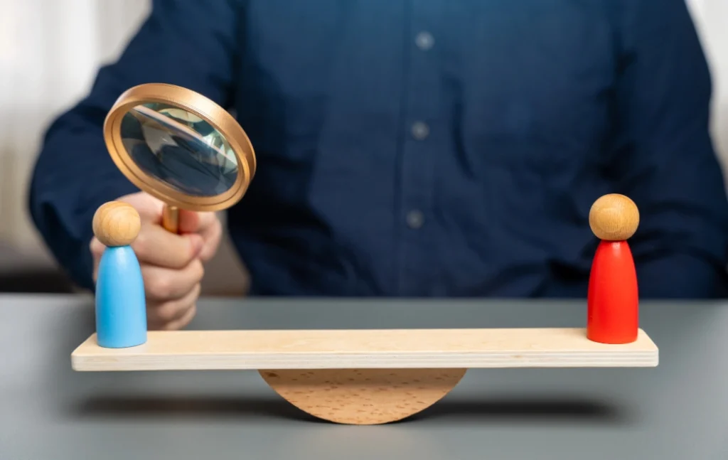 A balance scale with blue and red figurines, symbolizing the comparison between SEO and PPC services.