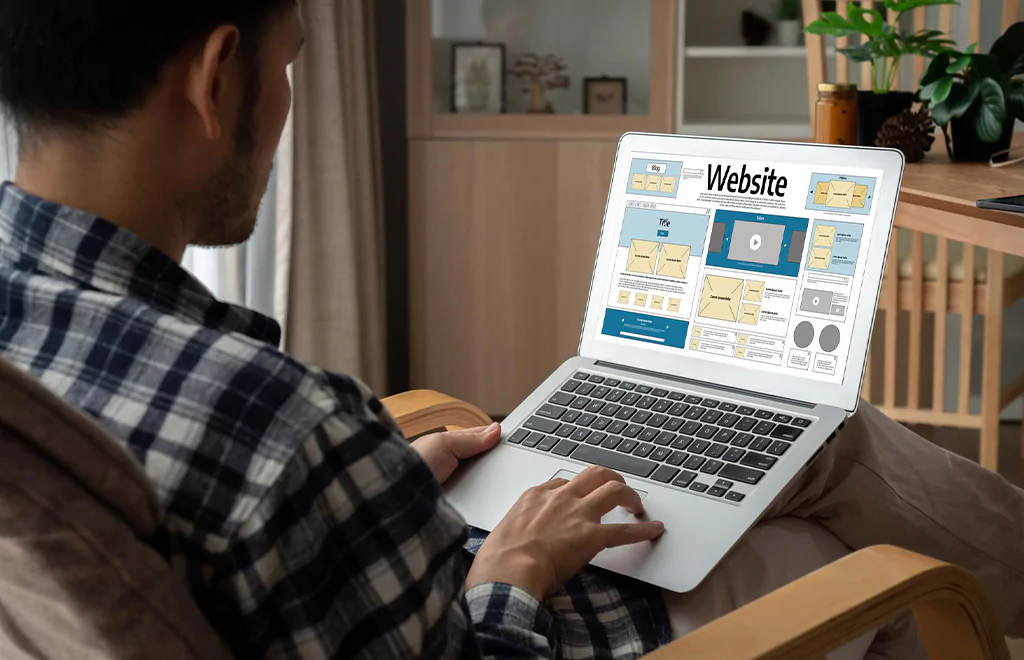 A person working on a website design layout on their laptop, displaying various website elements and content structure
