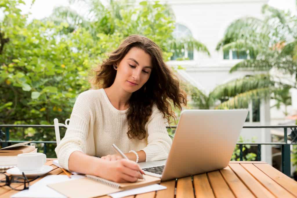 A woman hire a content writer while working on a laptop outdoors, surrounded by greenery and a relaxed environment