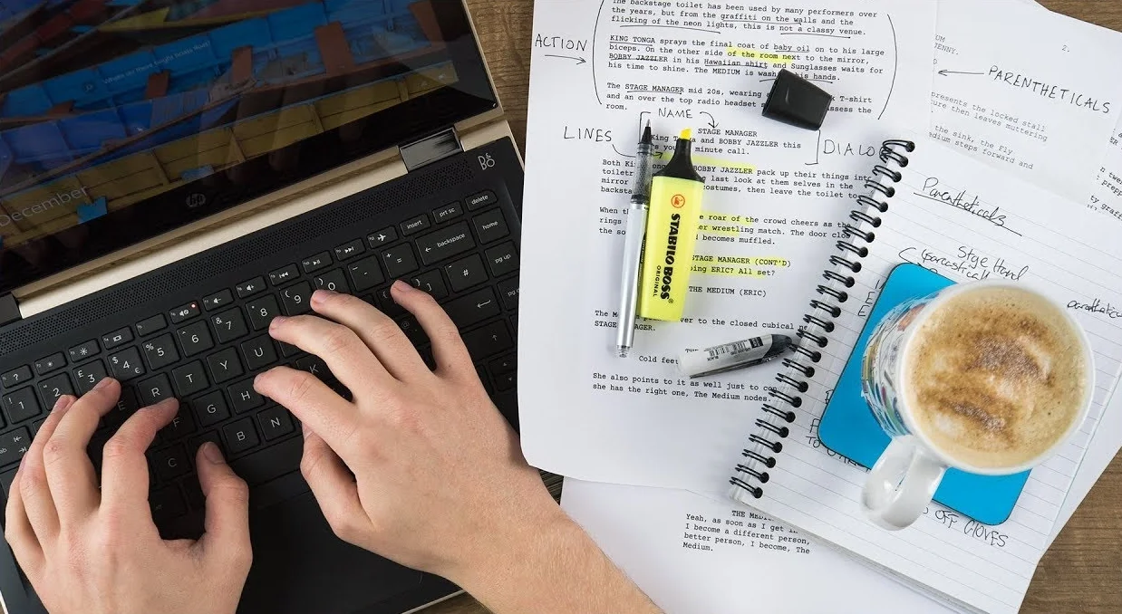 view of hands typing on laptop keyboard, highlighter and pen on paper, a cup of coffee