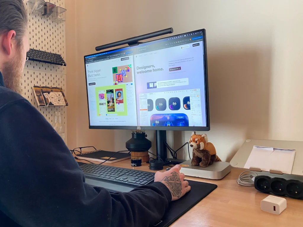 A person working at a desk with a computer, keyboard, and a plush fox toy.